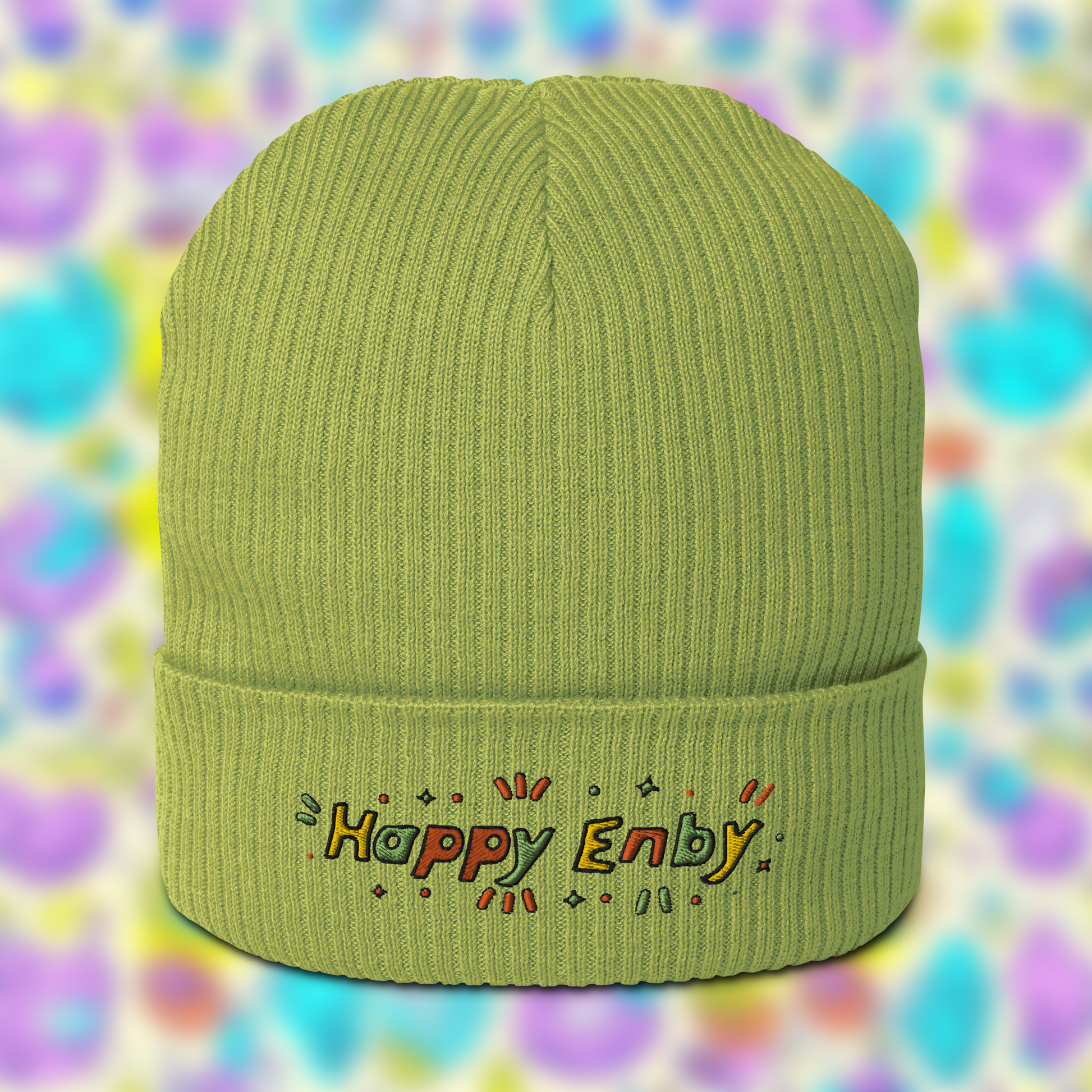 Light green beanie with embroidered text 'Happy Enby' in colourful letters, set against a blurred background of pastel colours.